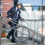Young,Businessman,In,Crash,Helmet,Carrying,Bicycle,Down,Steps